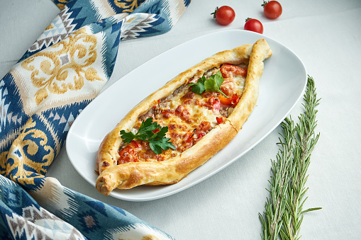 Close up view on traditional Turkish pide pie with sliced beef, tomatoes and melted cheese on white backgound. Turkish pizza